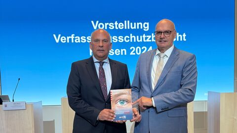 Roman Poseck und Bernd Neumann stehen nebeneinander und halten eine Broschüre in den Händen