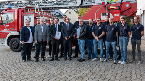 Innenminister Roman Poseck u.a. mit Bürgermeister Marcus Rahner, dem 1. Beigeordneten Günter Müller und Feuerwehrkameraden  Eine Gruppe von 16 Personen steht draußen vor einem Feuerwehrfahrzeug