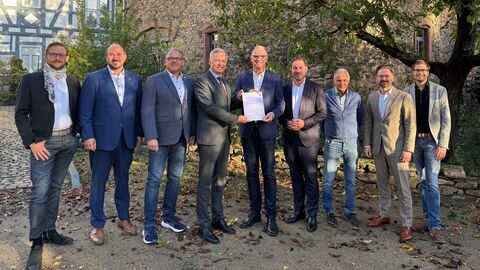 Innenstaatssekretär Rößler steht mit einer Gruppe Personen zur Bescheidübergabe in einem Innenhof neben einem Baum.