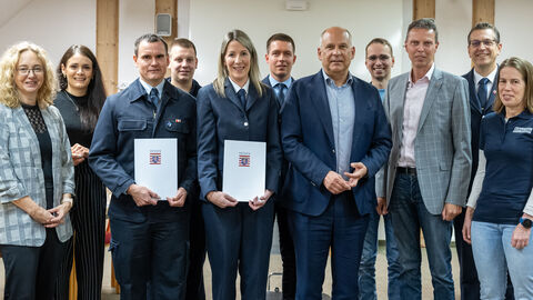 Eine Gruppe von ungefähr 10 Menschen stehen in einer Reihe - zwei halten jeweils einen Förderbescheid in den Händen