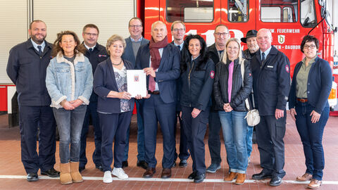 Eine Gruppe von 13 Personen steht vor einem Feuerwehrfahrzeug - zwei halten gemeinsam einen Förderbescheid in den Händen.