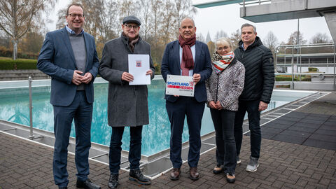 Fünf Personen stehen nebeneinander vor einem Außenschwimmbecken. 