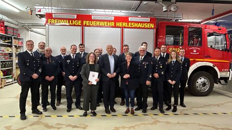 Innenminister Poseck mit einer Gruppe weiterer Personen in einer Feuerwehrhalle vor einem Feuerwehrfahrzeug bei der Bescheidübergabe