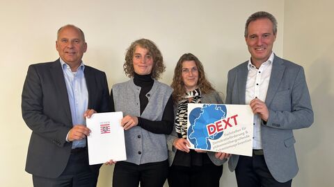 Vier Personen stehen zusammen und halten Förderbescheid in den Händen.