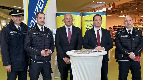 Drei Männer in Polizeiuniform und zwei Männer in Anzug stehen nebeneinander in einem Einkaufscenter