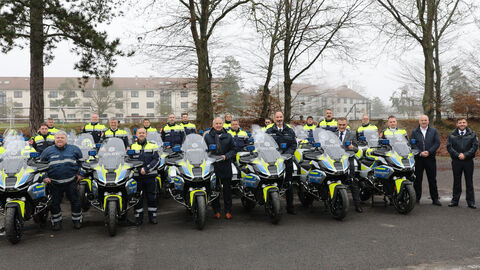 Der Innenminister steht mit circa 20 uniformierten Polizisten und ihren Motorrädern auf einem Parkplatz. 
