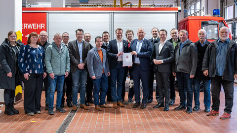 Eine Gruppe von Menschen steht vor einem Feuerwehrauto. In der Mitte steht der Innenminister und hält einen Zuwendungsbescheid in den Händen.