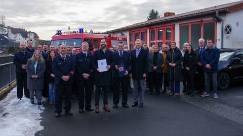 Eine Gruppe von circa 40 Personen steht vor einem Feuerwehrgebäude und einem Feuerwehrwagen.