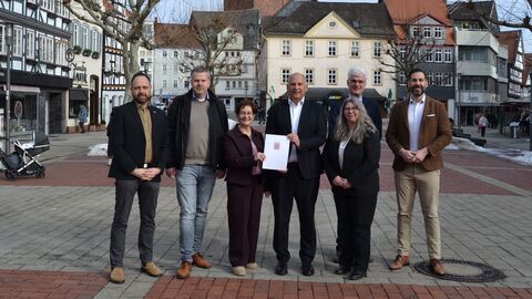 Sieben Personen stehen auf einem Marktplatz und zwei von ihnen halten gemeinsam einen Förderbescheid in den Händen