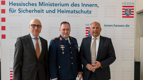 Drei Männer stehen vor großer Leinwand auf der steht: Hessische Ministerium des Innern, für Sicherheit und Heimatschutz 