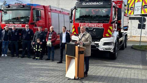 Minister Poseck steht an einem Rednerpult - hinter ihm stehen Personen der Feuerwehr und zwei Feuerwehrwagen 