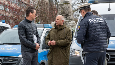 Roman Poseck steht mit Polizistinnen und Polizisten vor mehreren Polizeifahrzeugen.
