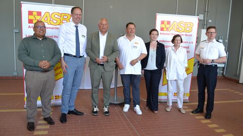Der Minister steht mit sechs weiteren Personen in einer Reihe - hinter ihnen zwei Aufsteller mit der Aufschrift "ASB Arbeiter- und Samariter-Bund