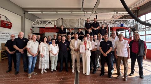 Mehr als 20 Personen stehen in einer Garage vor einem Feuerwehrauto.