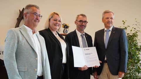 Herr Rößler steht mit drei weiteren Personen in einer Reihe - einer der Herren hält eine Urkunde in den Händen.