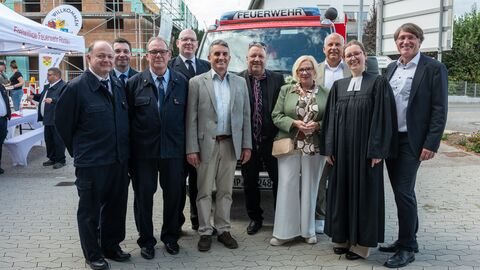Zehn Personen, darunter Herr Poseck, stehen gemeinsam auf einem Parkplatz vor einem kleinen Feuerwehrwagen