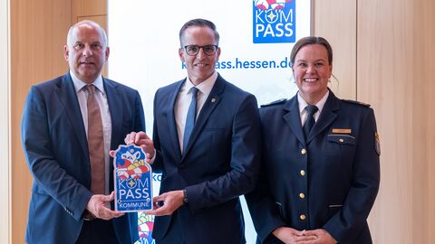 Herr Poseck steht neben zwei Männern - gemeinsam mit einem von ihnen hält er ein KOMPASS Siegel in den Händen