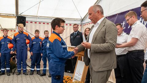 Herr Poseck übergibt einem Jugendlichen eine Urkunde und gibt ihm gleichzeitig die Hand - im Hintergrund viele weitere Jugendliche in Uniformen