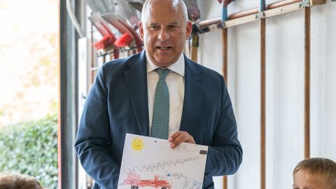 Herr Poseck hält ein von einem Kind gemaltes Bild in den Händen. Ein paar Kinder sitzen vor ihm und schauen ihn an.