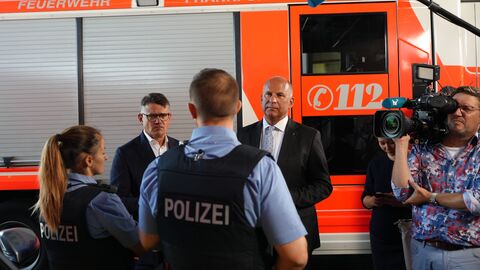 Innenminister Roman Poseck mit Ministerpräsident Boris Rhein im Gespräch mit Polizistinnen und Polizisten. Im Hintergrund ein Feuerwehrauto.